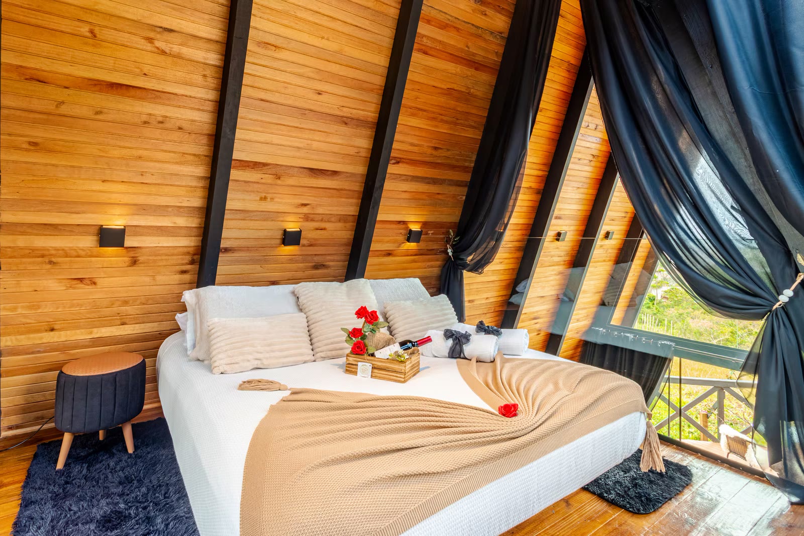 Quarto do chalé com cama arrumada, vinho e rosa, sob o teto A-frame
