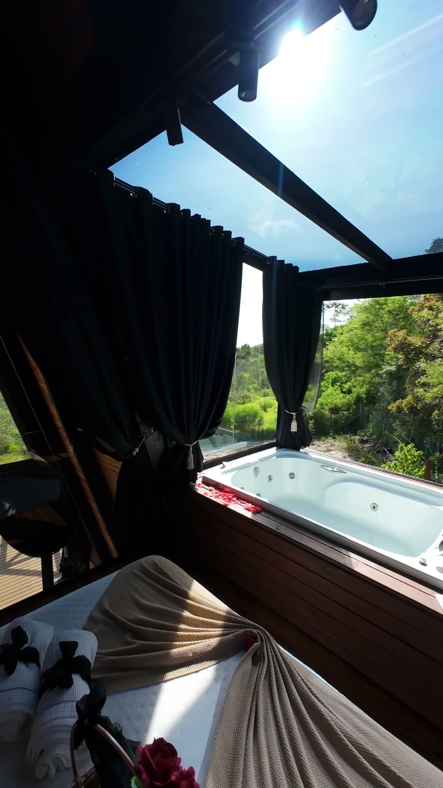Banheira de hidromassagem sob cortinas escuras, com vista para a natureza