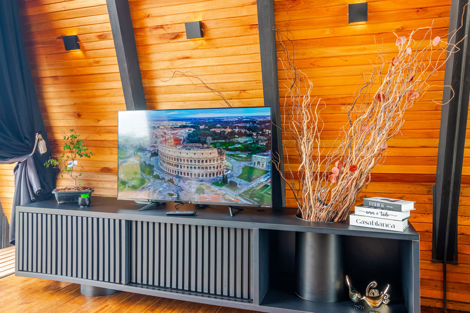Sala com TV e painel de madeira, iluminada por arandelas